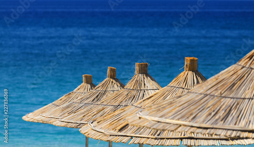 Close-up of reed beach umbrellas on a turquoise warm sea background.