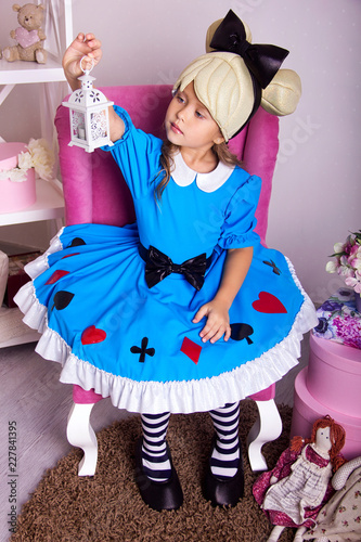 little girl in blue dress. kid christmas halloween costume. young happy girl in white room is sitting and looking to the lamp in her hand in pink armchair with beauty smile near gifts