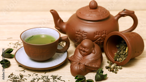 Зеленый чай в керамической чашке и чайнике, фигурка будды 