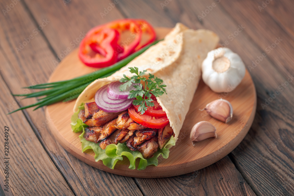 Doner kebab is lying on the cutting board. Shawarma with chicken meat, onions, salad lies on a dark old wooden table.
