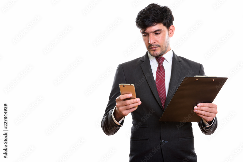 Studio shot of young Persian businessman holding clipboard while Studio shot of young Persian businessman holding clipboard while