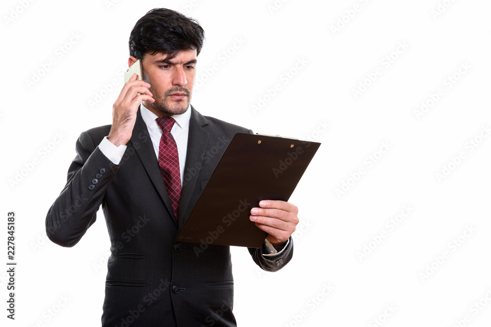 Studio shot of young Persian businessman reading on clipboard wh Studio shot of young Persian businessman reading on clipboard wh