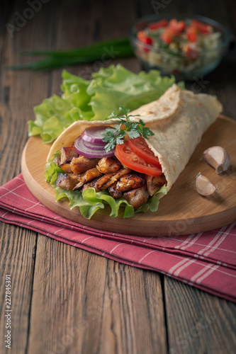 Doner kebab is lying on the cutting board. Shawarma with chicken meat, onions, salad lies on a dark old wooden table.