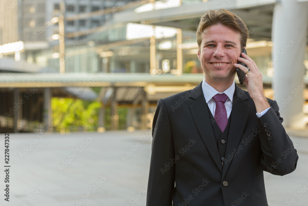 Happy businessman smiling and talking on mobile phone in front o Happy businessman smiling and talking on mobile phone in front o