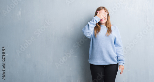 Young adult woman over grey grunge wall wearing glasses smiling and laughing with hand on face covering eyes for surprise. Blind concept.