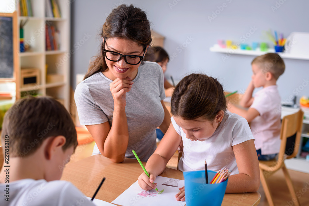 Fototapeta premium Nauczyciel przedszkola patrzy na inteligentne dziecko uczące się pisać i rysować. Wczesna edukacja. Wykorzystanie kreatywności i wsparcia.