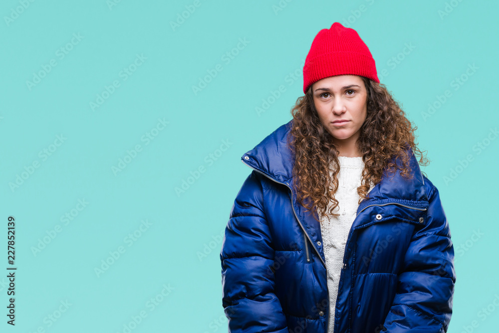 Beautiful young brunette curly hair girl wearing winter coat, wool cap and sweater over isolated background with serious expression on face. Simple and natural looking at the camera. Beautiful young brunette curly hair girl wearing winter coat, wool cap and sweater over isolated background with serious expression on face. Simple and natural looking at the camera.
