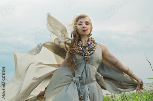 Fotografia elf or fairy walks among the summer grasses in a grey dress swollen in the wind