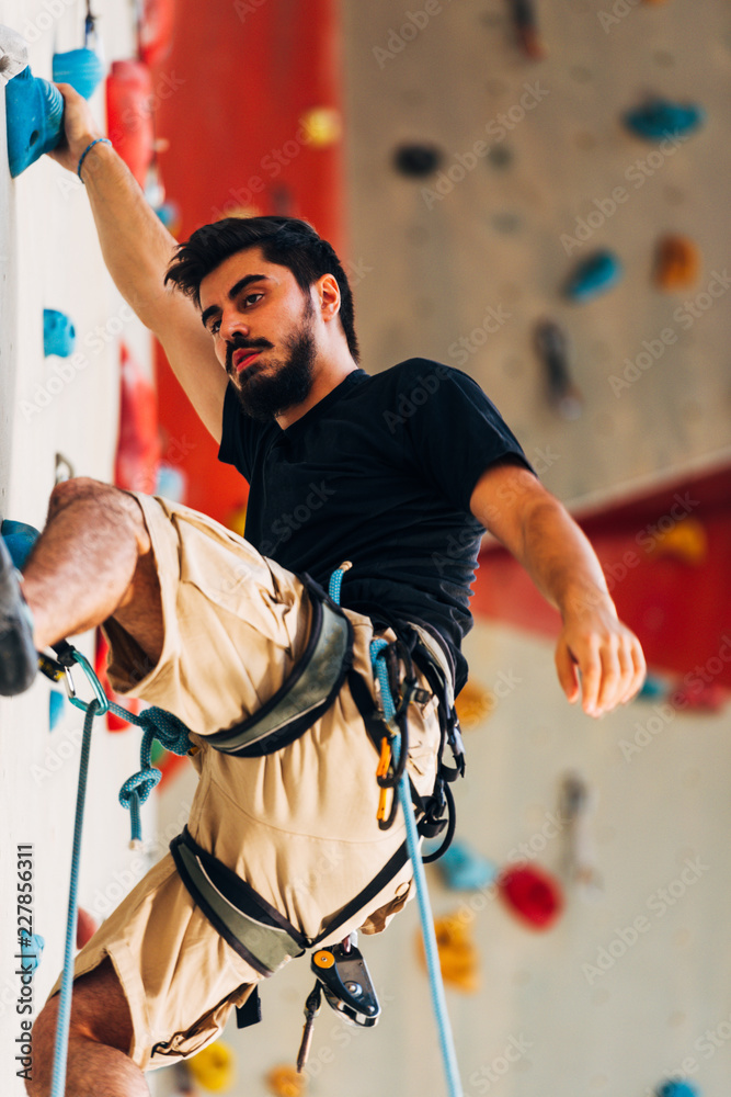 Sportive man climbs up on artificial rock wall