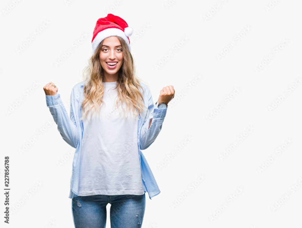 Beautiful young blonde woman wearing christmas hat over isolated background celebrating surprised and amazed for success with arms raised and open eyes. Winner concept. Beautiful young blonde woman wearing christmas hat over isolated background celebrating surprised and amazed for success with arms raised and open eyes. Winner concept.