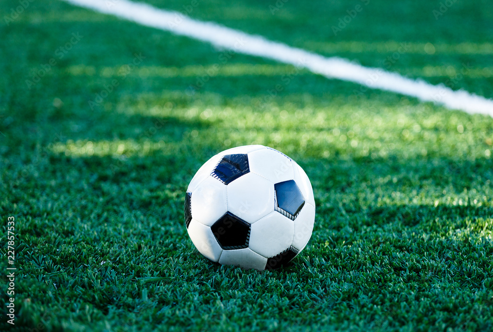 Obraz premium classical black and white football ball on the green grass of the field. Soccer game, training, hobby concept. with copy space 