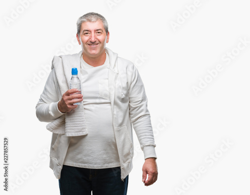 Handsome senior man training holding towel and water bottle over isolated background with a happy face standing and smiling with a confident smile showing teeth