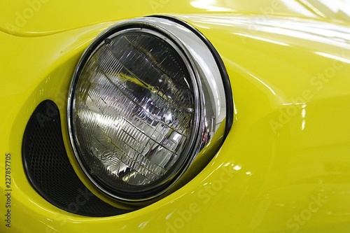 Round head light and part of front mask of small ibright yellow talian coupe veteran car dated to 1965 photo