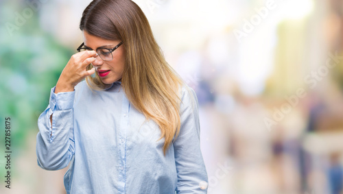 Young beautiful business woman wearing glasses over isolated background tired rubbing nose and eyes feeling fatigue and headache. Stress and frustration concept. © Krakenimages.com