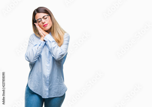 Young beautiful business woman wearing glasses over isolated background sleeping tired dreaming and posing with hands together while smiling with closed eyes. © Krakenimages.com