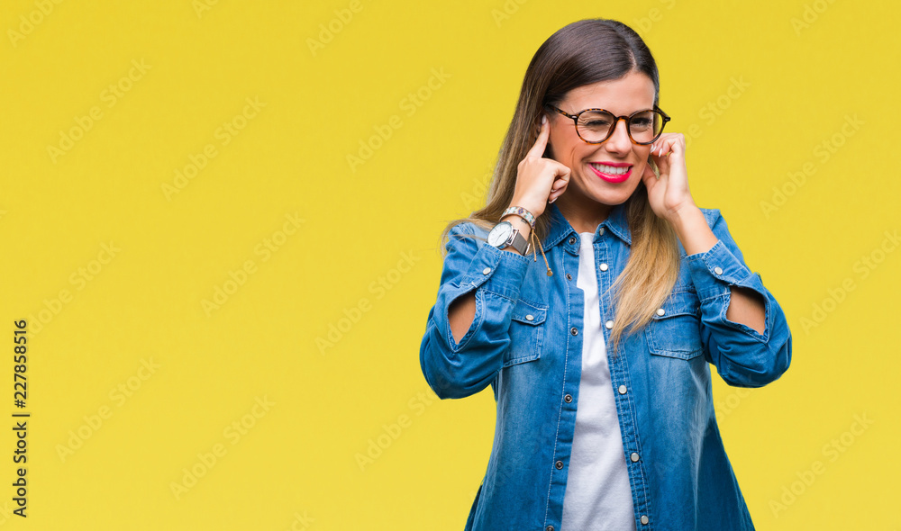 Young beautiful woman over wearing glasses over isolated background covering ears with fingers with annoyed expression for the noise of loud music. Deaf concept. Young beautiful woman over wearing glasses over isolated background covering ears with fingers with annoyed expression for the noise of loud music. Deaf concept.