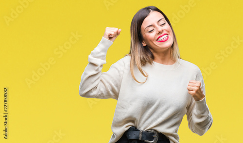 Young beautiful woman casual white sweater over isolated background very happy and excited doing winner gesture with arms raised, smiling and screaming for success. Celebration concept.