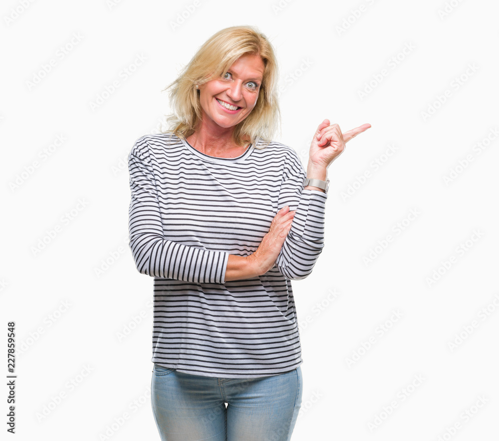 Middle age blonde woman over isolated background with a big smile on face, pointing with hand and finger to the side looking at the camera. Middle age blonde woman over isolated background with a big smile on face, pointing with hand and finger to the side looking at the camera.
