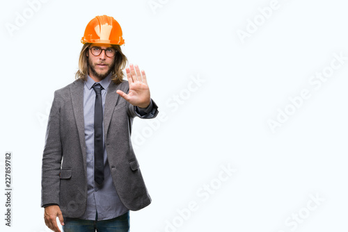 Young handsome architec man with long hair wearing safety helmet over isolated background doing stop sing with palm of the hand. Warning expression with negative and serious gesture on the face. © Krakenimages.com