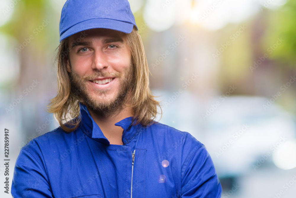 Young handsome mechanic man with long hair over isolated background happy face smiling with crossed arms looking at the camera. Positive person. Young handsome mechanic man with long hair over isolated background happy face smiling with crossed arms looking at the camera. Positive person.