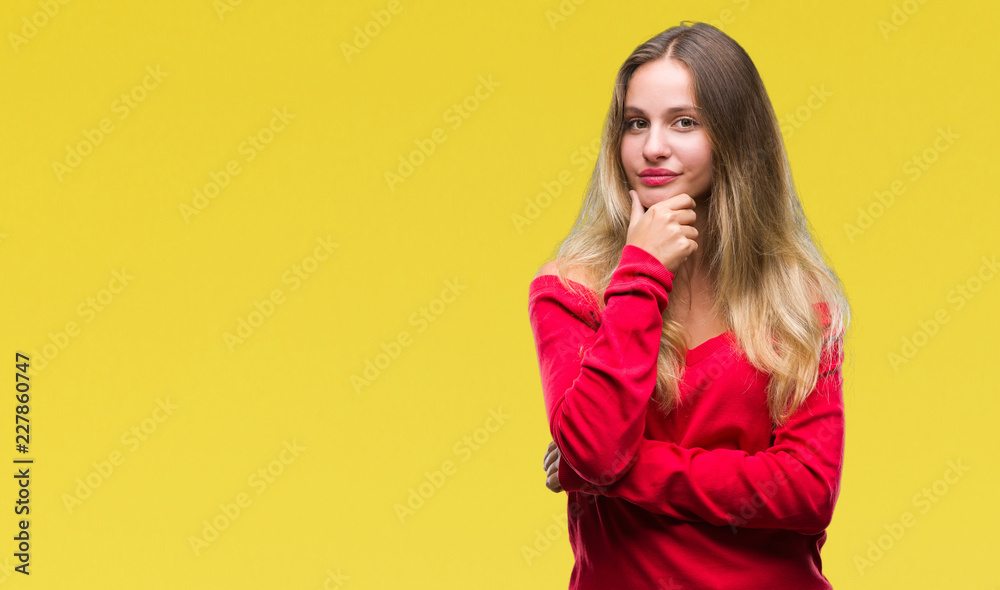 Fototapeta premium Young beautiful blonde woman wearing red sweater over isolated background looking confident at the camera with smile with crossed arms and hand raised on chin. Thinking positive.