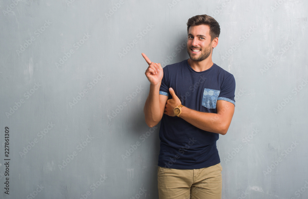 Handsome young man over grey grunge wall with a big smile on face, pointing with hand and finger to the side looking at the camera. Handsome young man over grey grunge wall with a big smile on face, pointing with hand and finger to the side looking at the camera.