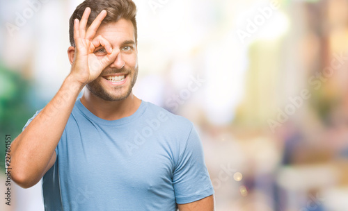 Young handsome man over isolated background doing ok gesture with hand smiling, eye looking through fingers with happy face.
