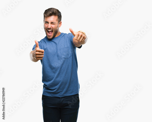 Young handsome man over isolated background approving doing positive gesture with hand, thumbs up smiling and happy for success. Looking at the camera, winner gesture.