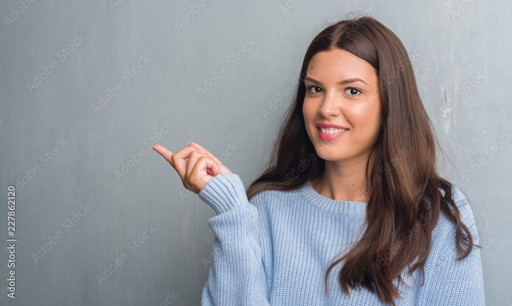 Young brunette woman over grunge grey wall very happy pointing with hand and finger to the side Young brunette woman over grunge grey wall very happy pointing with hand and finger to the side