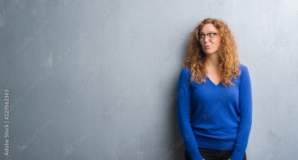 Young redhead woman over grey grunge wall smiling looking side and staring away thinking.