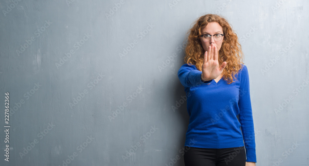 Fototapeta premium Young redhead woman over grey grunge wall doing stop sing with palm of the hand. Warning expression with negative and serious gesture on the face.