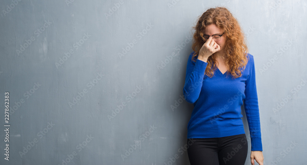 Young redhead woman over grey grunge wall tired rubbing nose and eyes feeling fatigue and headache. Stress and frustration concept. Young redhead woman over grey grunge wall tired rubbing nose and eyes feeling fatigue and headache. Stress and frustration concept.