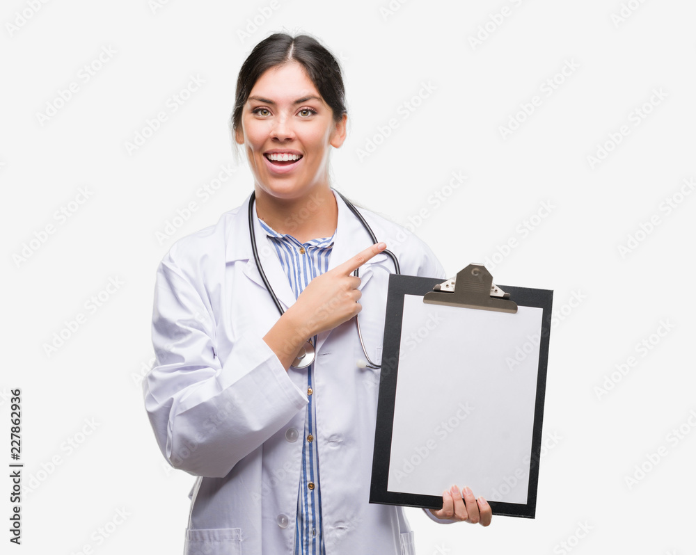 Young hispanic doctor woman holding clipboard very happy pointing with hand and finger to the side Young hispanic doctor woman holding clipboard very happy pointing with hand and finger to the side