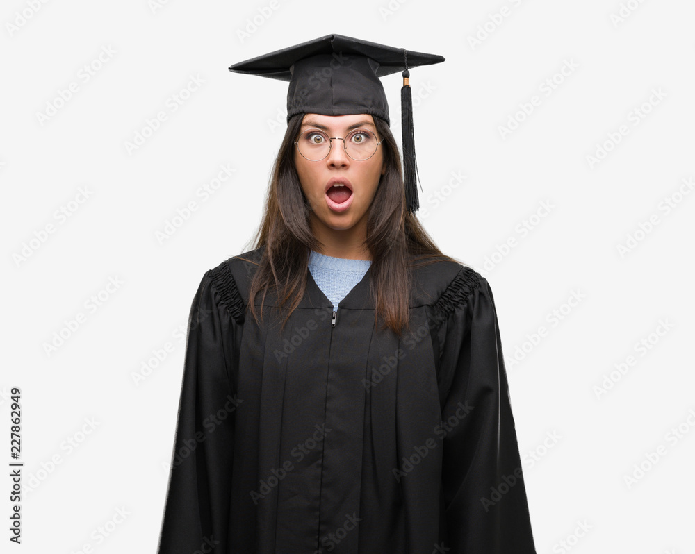 Young hispanic woman wearing graduated cap and uniform afraid and shocked with surprise expression, fear and excited face.