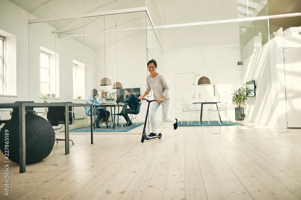 Smiling young Asian businesswoman riding a scooter around an off