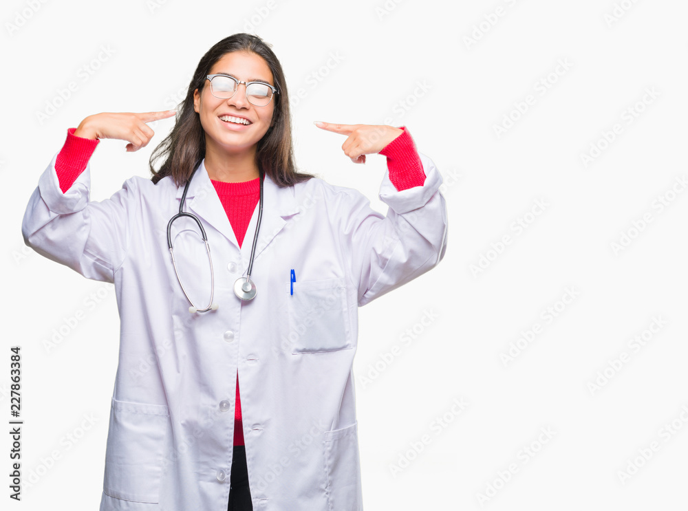 Young arab doctor woman over isolated background smiling confident showing and pointing with fingers teeth and mouth. Health concept. Young arab doctor woman over isolated background smiling confident showing and pointing with fingers teeth and mouth. Health concept.