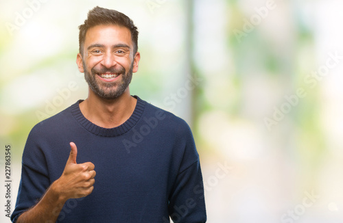 Adult hispanic man over isolated background doing happy thumbs up gesture with hand. Approving expression looking at the camera with showing success. © Krakenimages.com