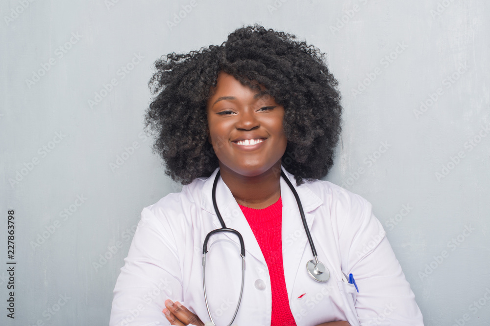 Young african american doctor woman over grey grunge wall happy face smiling with crossed arms looking at the camera. Positive person. Young african american doctor woman over grey grunge wall happy face smiling with crossed arms looking at the camera. Positive person.