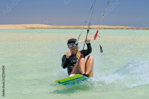 Kite surfing girl in sexy swimsuit with kite in sky on board in blue sea riding waves with water splash. Recreational activity, water sports, action, hobby and fun in summer time. Kiteboarding sport