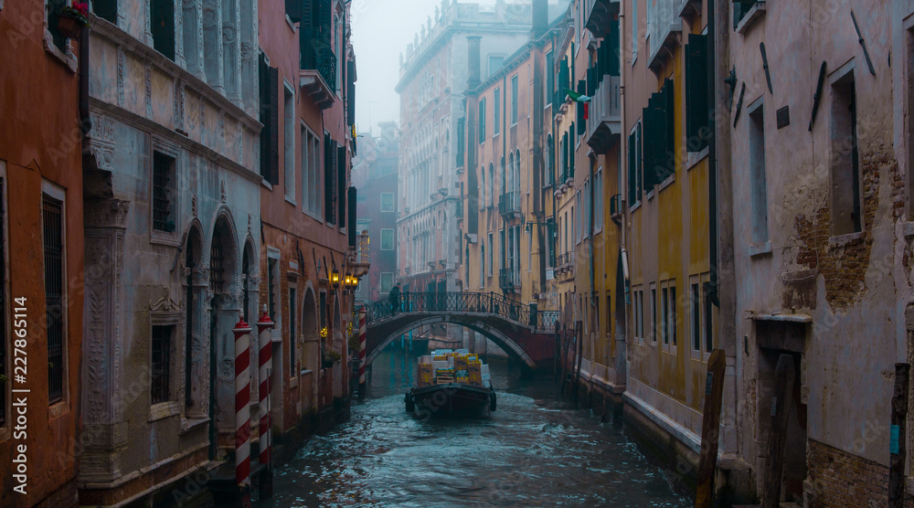 Single boat cruising on a canal in Venice Italy, winter foggy morning