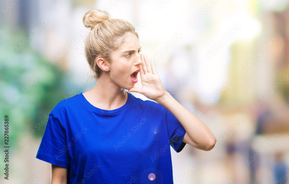 Young beautiful blonde and blue eyes woman wearing blue t-shirt over isolated background shouting and screaming loud to side with hand on mouth. Communication concept.