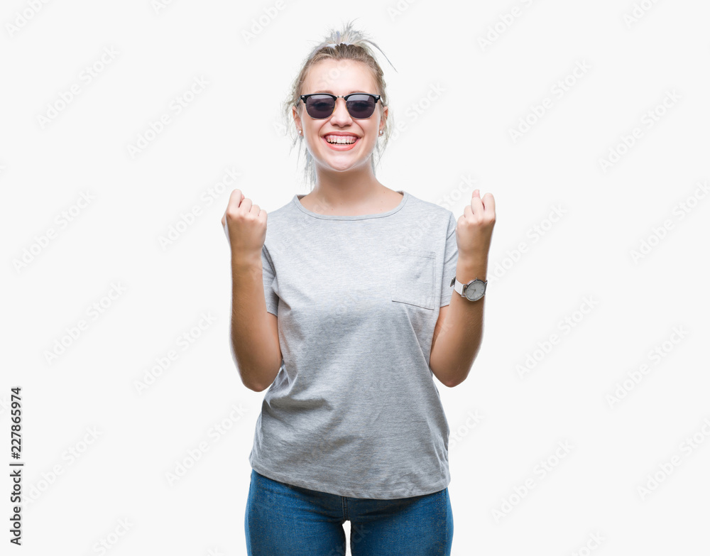 Young blonde woman wearing sunglasses over isolated background celebrating surprised and amazed for success with arms raised and open eyes. Winner concept. Young blonde woman wearing sunglasses over isolated background celebrating surprised and amazed for success with arms raised and open eyes. Winner concept.