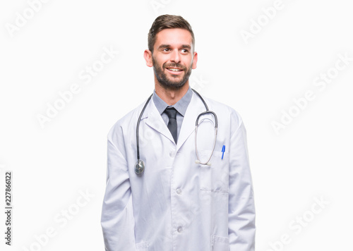 Young handsome doctor man over isolated background looking away to side with smile on face, natural expression. Laughing confident. © Krakenimages.com