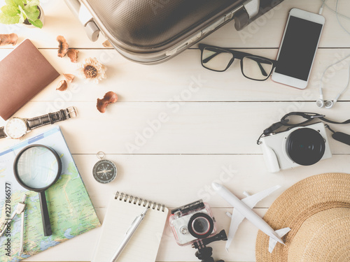 top view travel concept with digital camera, smartphone, map, passport, compass, action camera, luggage and Outfit of traveler on wooden background, Tourist essentials