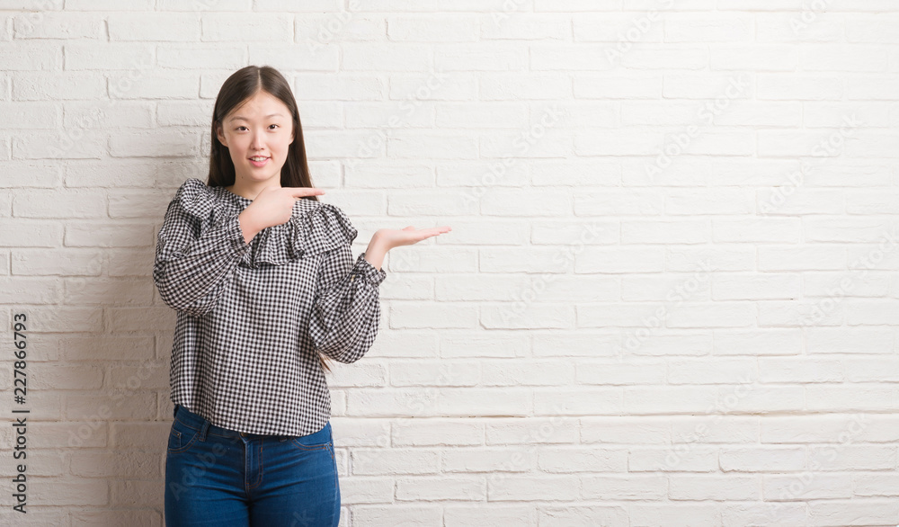 Young Chinese woman over brick wall very happy pointing with hand and finger Young Chinese woman over brick wall very happy pointing with hand and finger