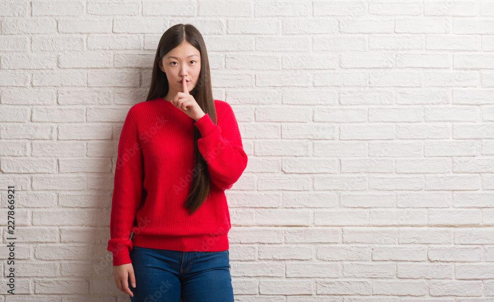 Young Chinese woman over brick wall asking to be quiet with finger on lips. Silence and secret concept. Young Chinese woman over brick wall asking to be quiet with finger on lips. Silence and secret concept.