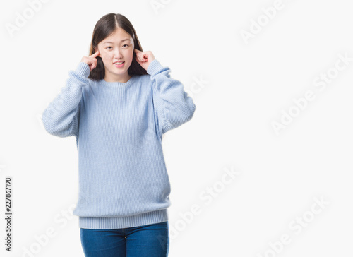 Young Chinese woman over isolated background covering ears with fingers with annoyed expression for the noise of loud music. Deaf concept. © Krakenimages.com