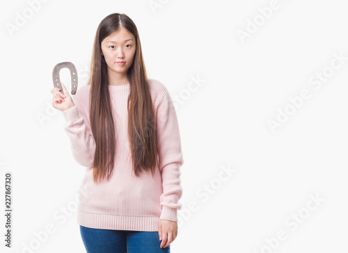 Young Chinese woman over isolated background holding horseshoe talisman with a confident expression on smart face thinking serious