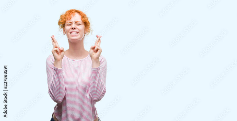 Young redhead woman smiling crossing fingers with hope and eyes closed. Luck and superstitious concept. Young redhead woman smiling crossing fingers with hope and eyes closed. Luck and superstitious concept.