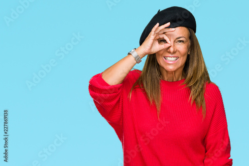 Middle age adult woman wearing fashion beret over isolated background doing ok gesture with hand smiling, eye looking through fingers with happy face.